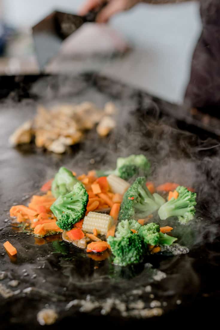 An assortment of vegetables and chicken pieces cooking on a Blackstone Griddle.