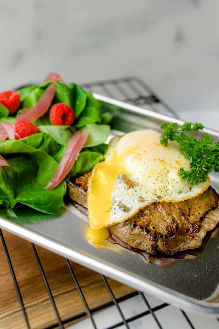 Blackstone Steak and Eggs on a small metal pan with a side salad all on a wire rack.
