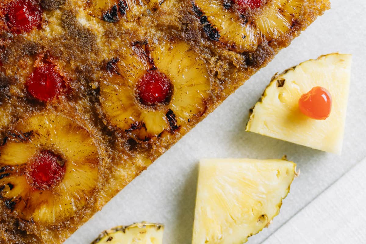 Homemade Grilled Pineapple Up-side Down Cake on a cutting board with fresh pineapple and cherry pieces.