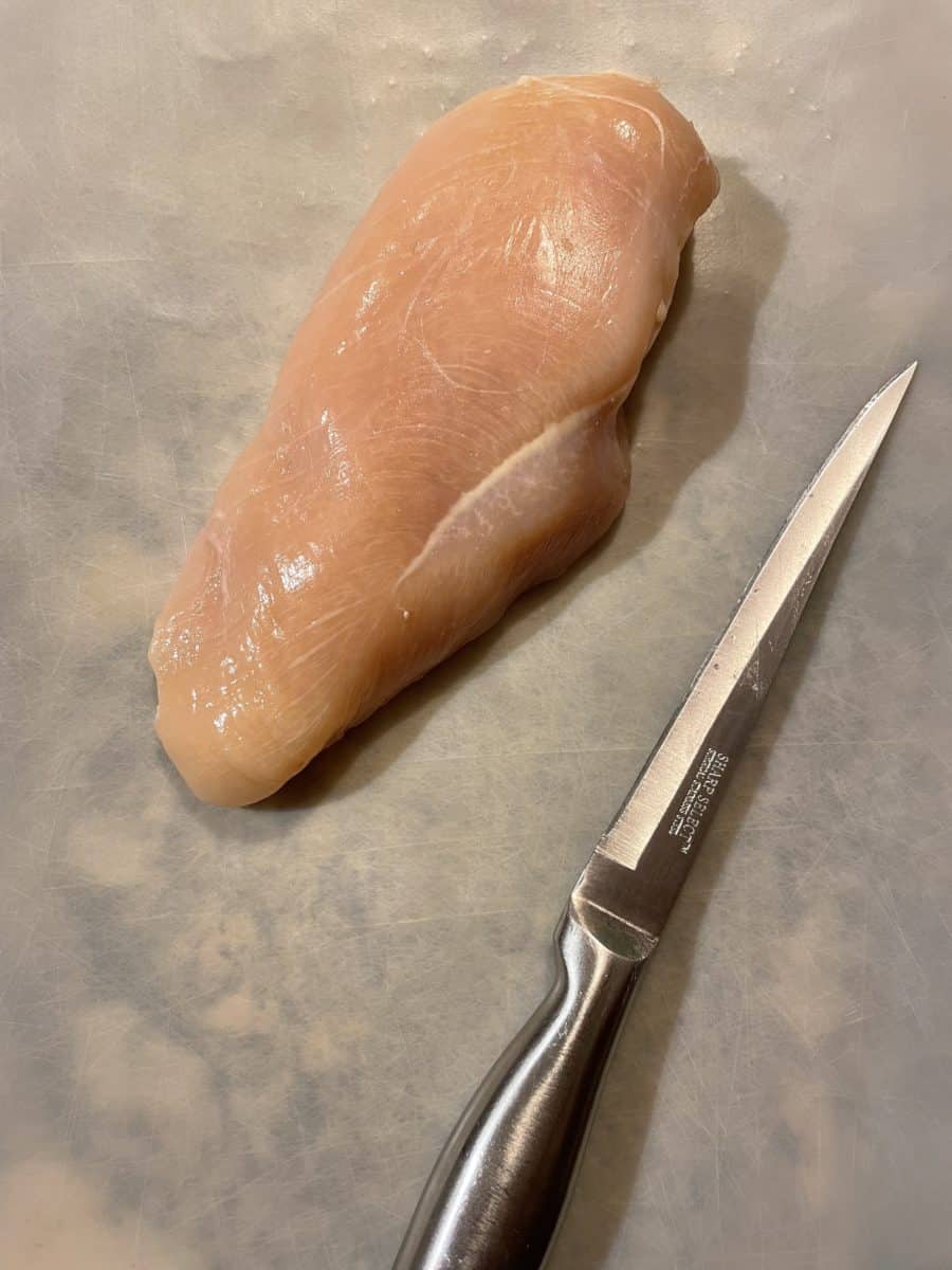 Cleaned Raw Chicken Breast on a cutting mat with a sharp knife.