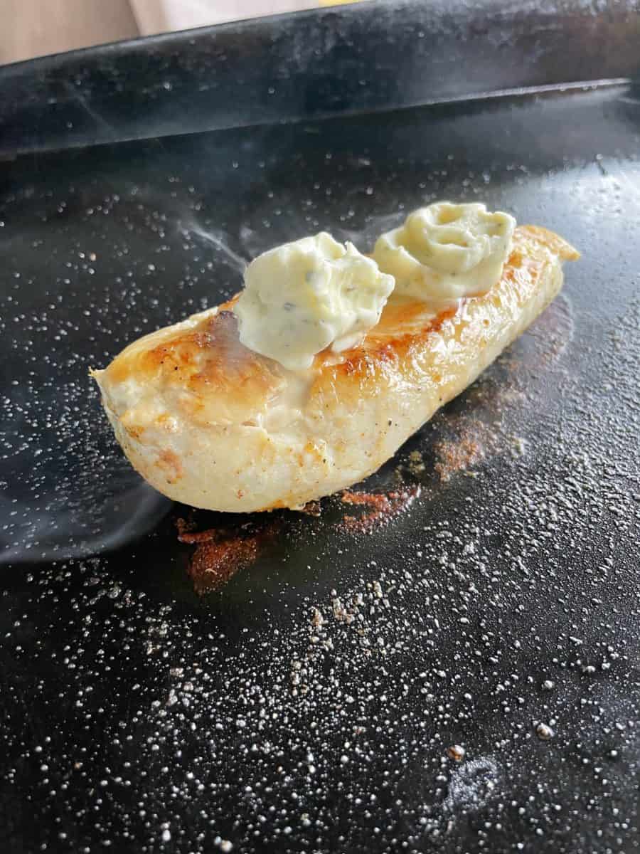 Adding Garlic Herb Butter to the top of a Griddle Chicken Breast.