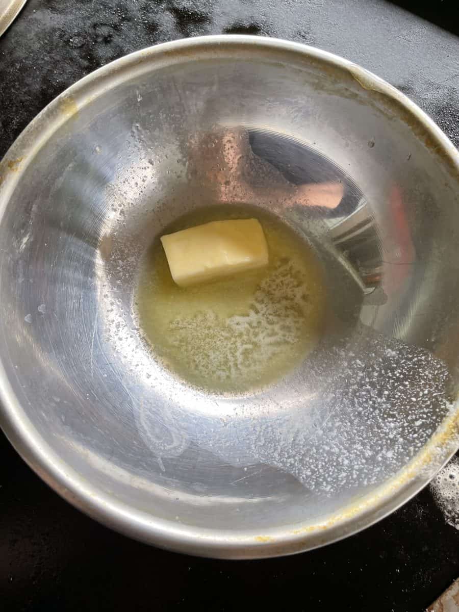Melted Butter in a Medium Sized Metal Bowl on top of a Blackstone Griddle.