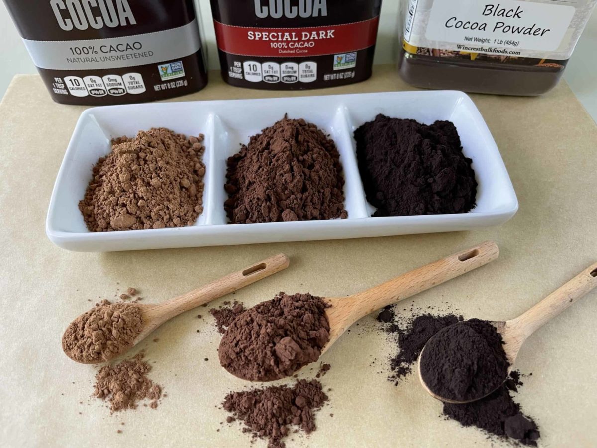Unsweetened Cocoa Powders - Regular, Dark, and Black Cocoa in a bowl, on wooden spoons, and in their serving containers.