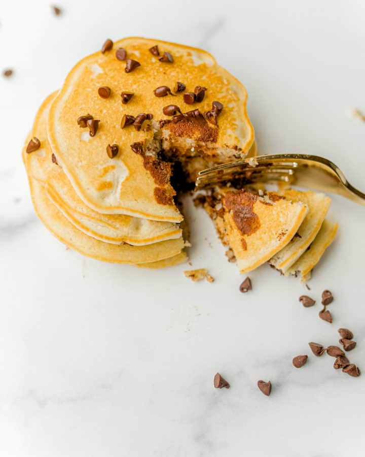 Chocolate Chip Pancakes stacked up and sprinkled with more chocolate chips and cut with a fork.