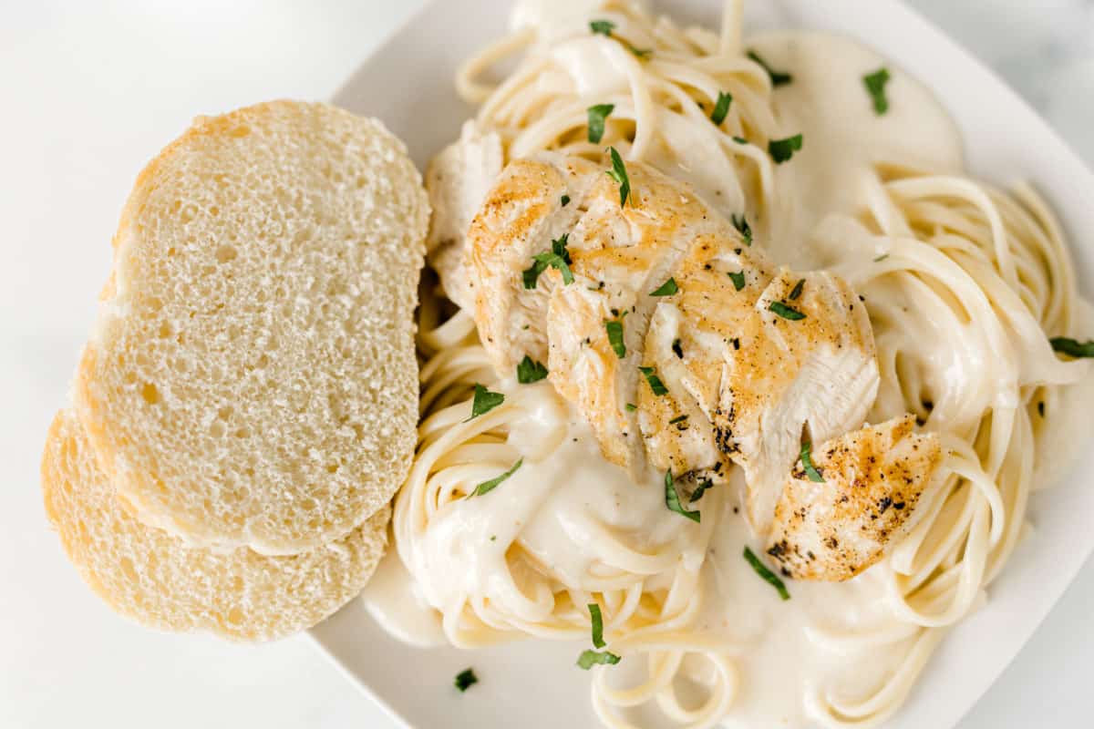 Chicken Fettuccine Alfredo Recipe with a couple slices of Italian bread on the side of a white plate.