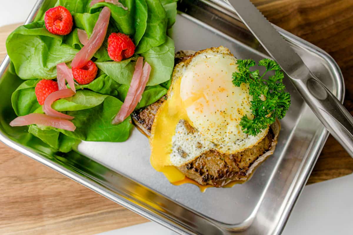 Steak and Eggs on a metal tray with a side salad all on a wooden board.