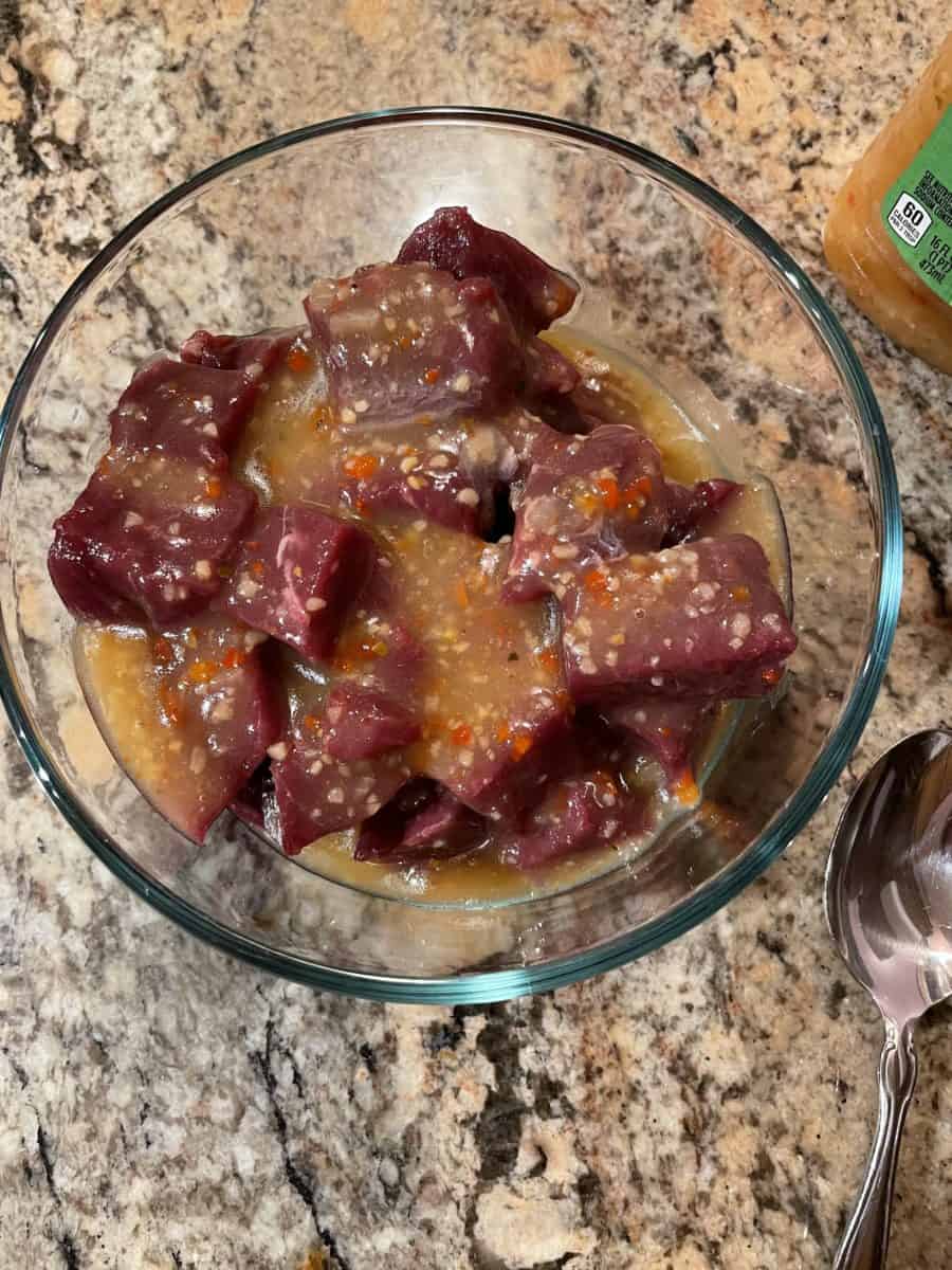Pieces of Venison Meat in a bowl topped with Italian dressing.