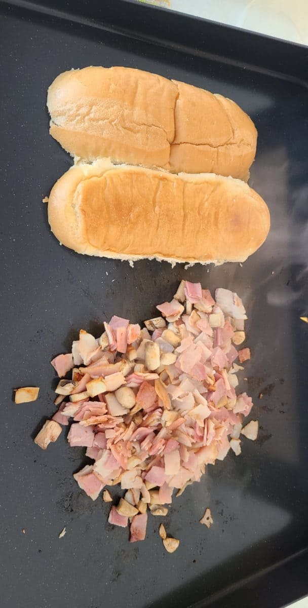 Sauteed deli ham and turkey along with mushroom and a sub bun on a hot griddle.