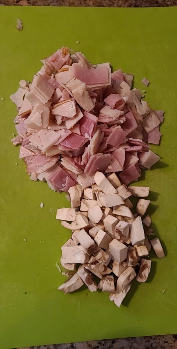 Diced ham, turkey, and mushrooms on a cutting mat.