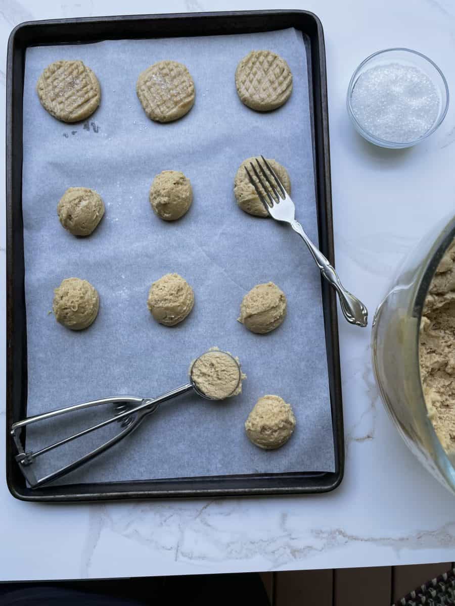 Portioning out Peanut Butter Cookie Dough on a baking sheet with a scooper and fork.