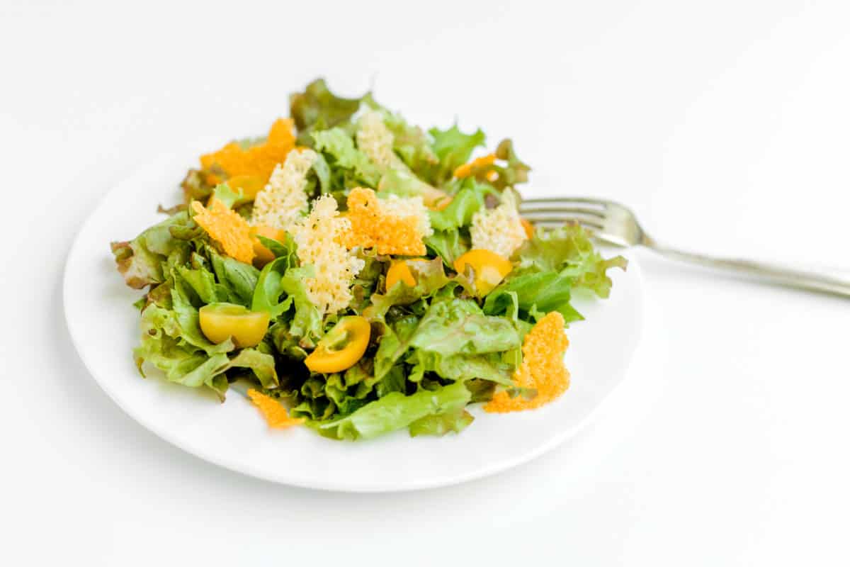 Green Leafy Salad Topped with Cheese Crisps on a white plate with a fork.