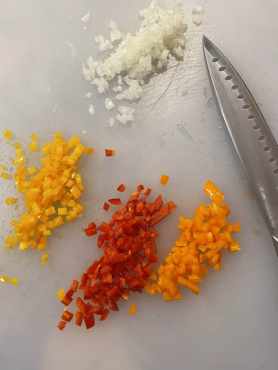Diced Vegetables on a cutting board - sweet peppers (orange, yellow, red) and white onion.