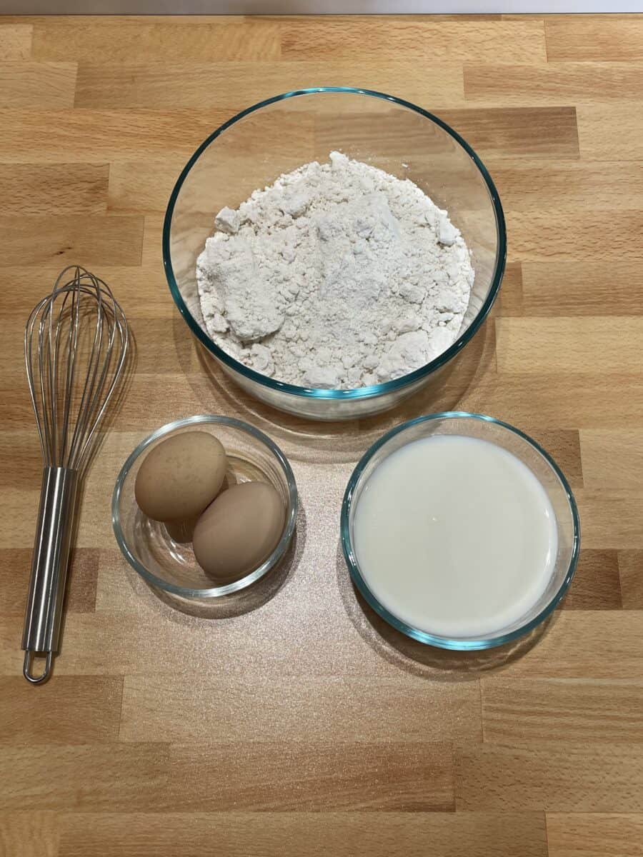 Bisquick Pancake Ingredients - Bisquick mix, milk, and eggs along with a whisk.