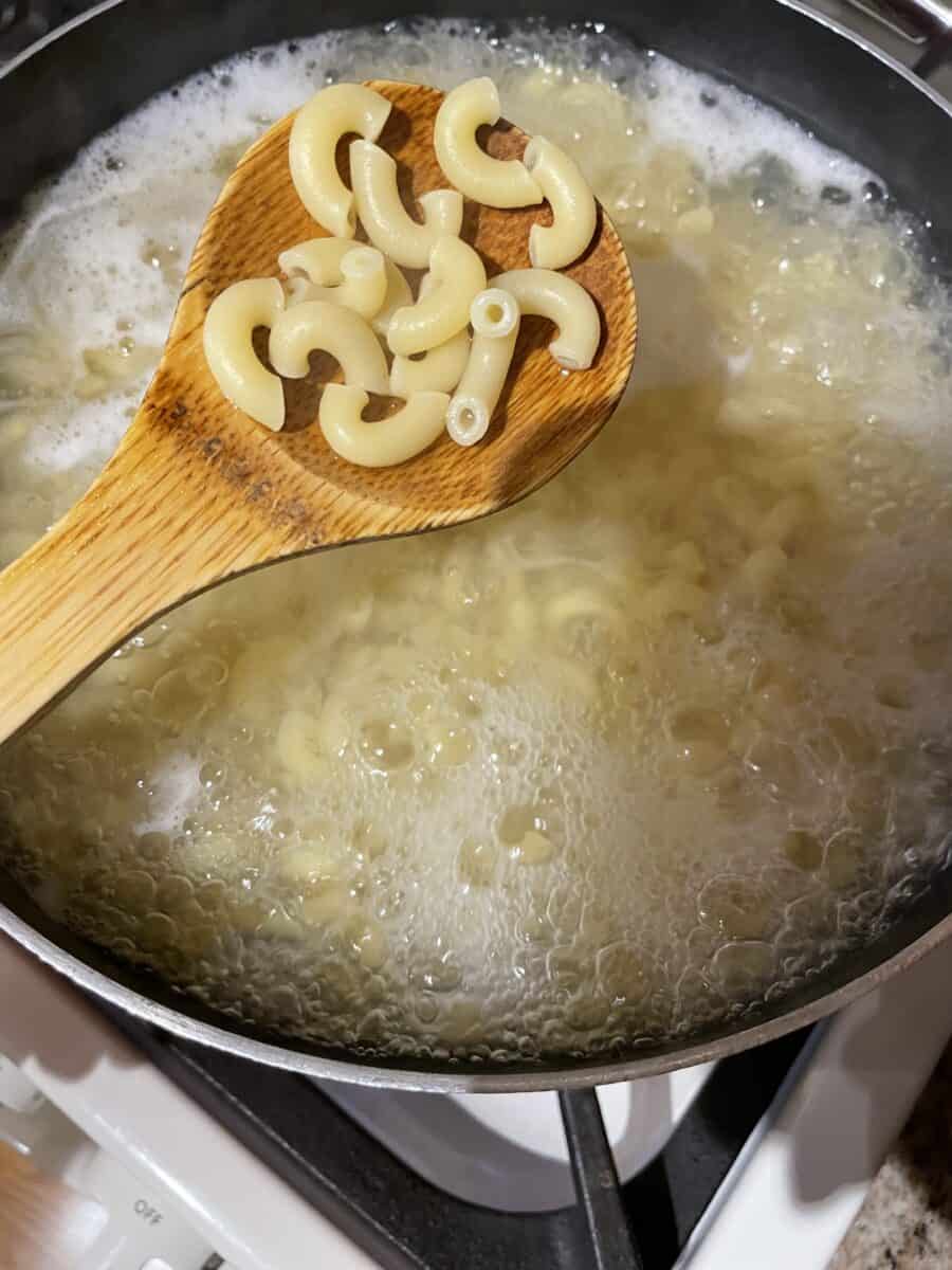 Cooking elbow macaroni in a large pot of boiling water.