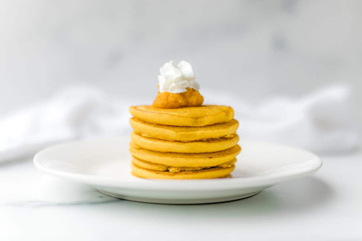Pumpkin Pancakes with Bisquick stacked on a plate topped with pumpkin puree and a squirt of whipped cream.