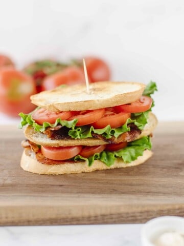 Blackstone BLT Sandwich on a wooden board with a bunch of tomatoes in the background.