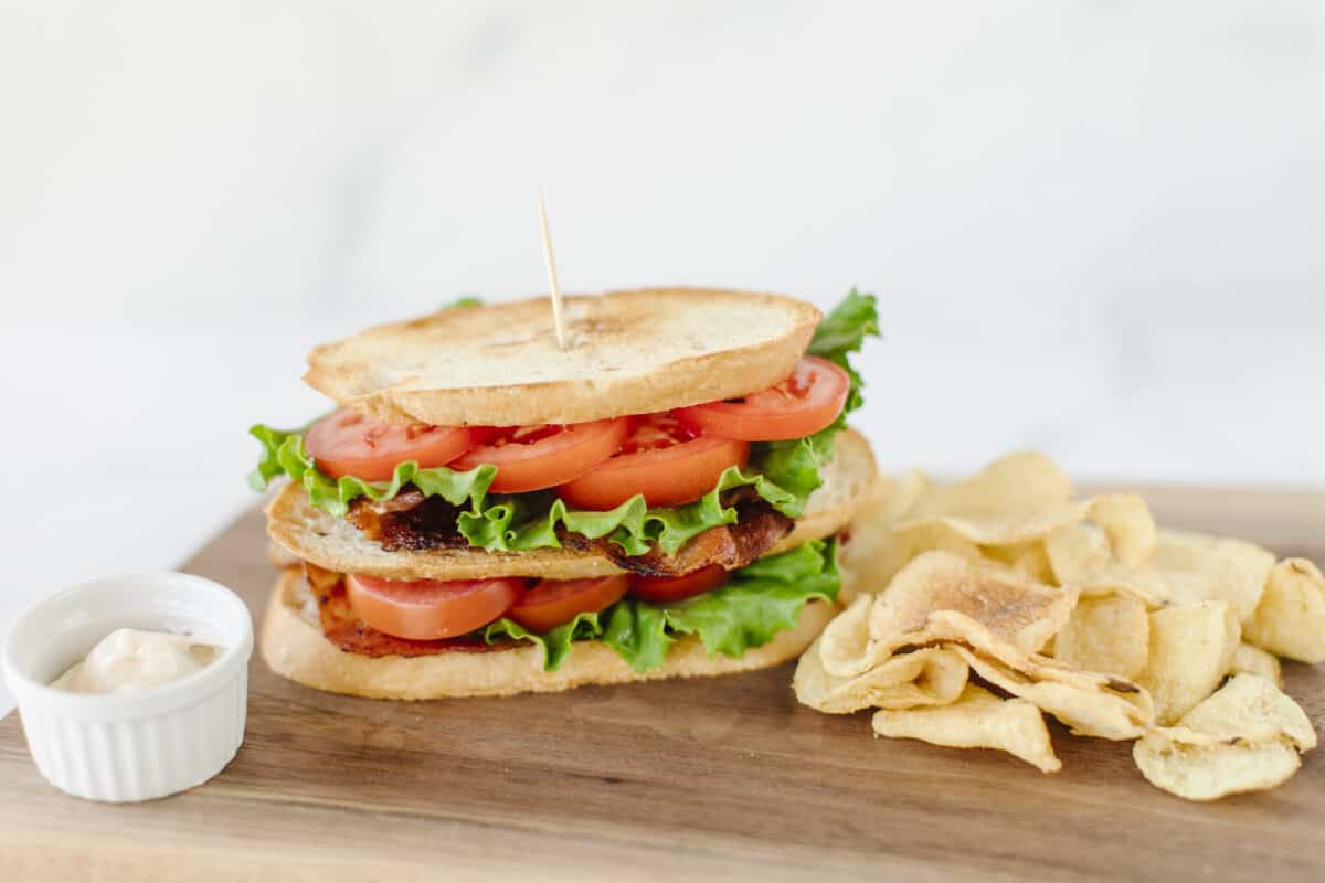 BLT Sandwich on a wooden board with a side of potato chips.