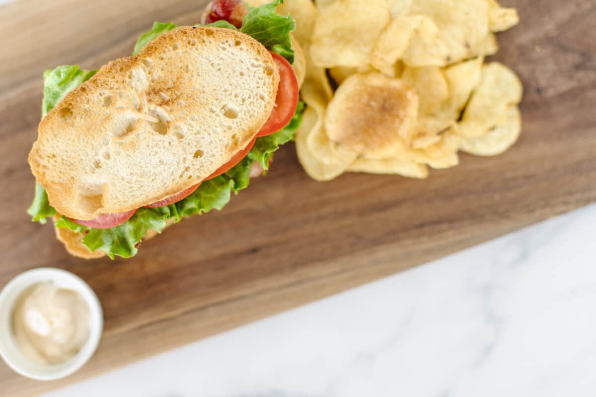 Toasted bread for a classic BLT sandwich on a wooden board with a side of potato chips.