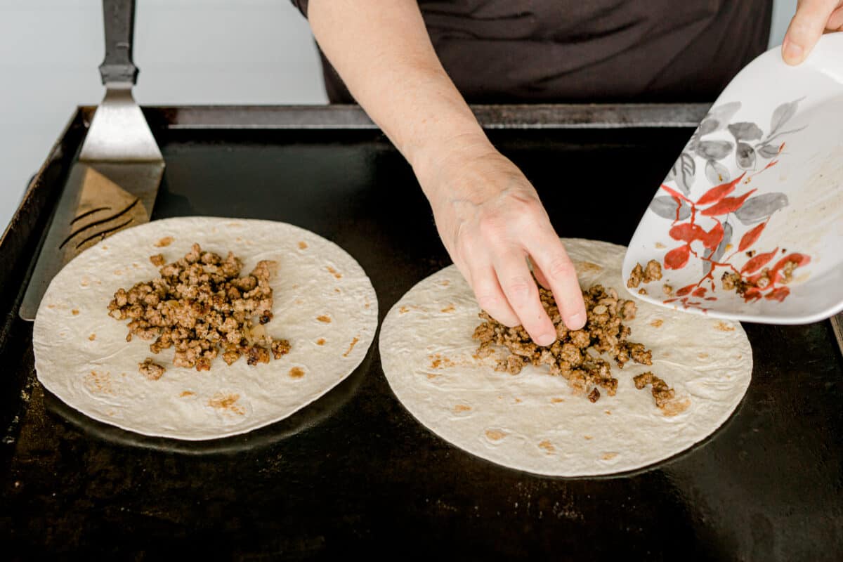 Adding the cooked burger to the top of a soft shell tortilla.