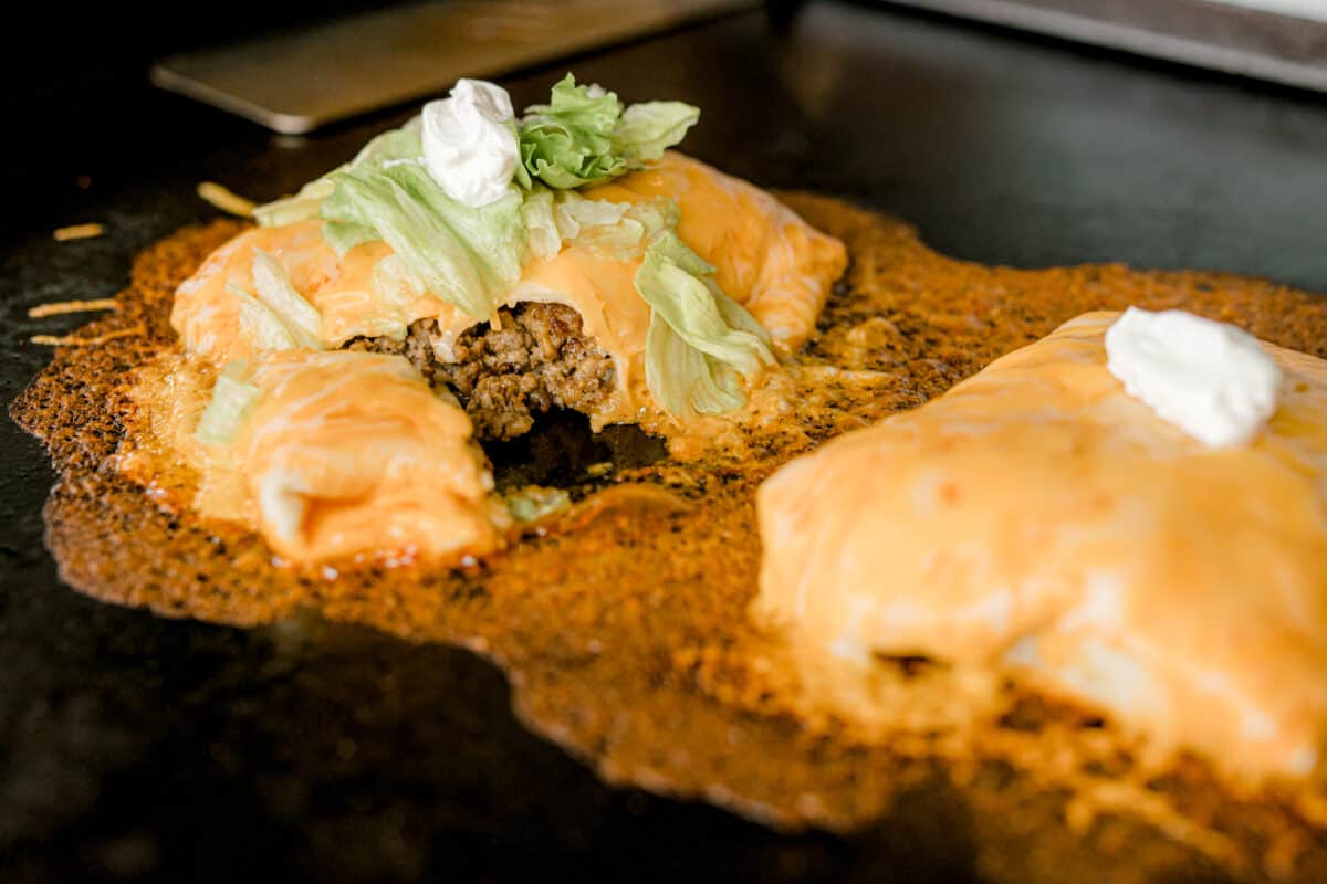 Blackstone Griddle Wet Burrito cooking and topped with shredded lettuce and a dollop of sour cream.