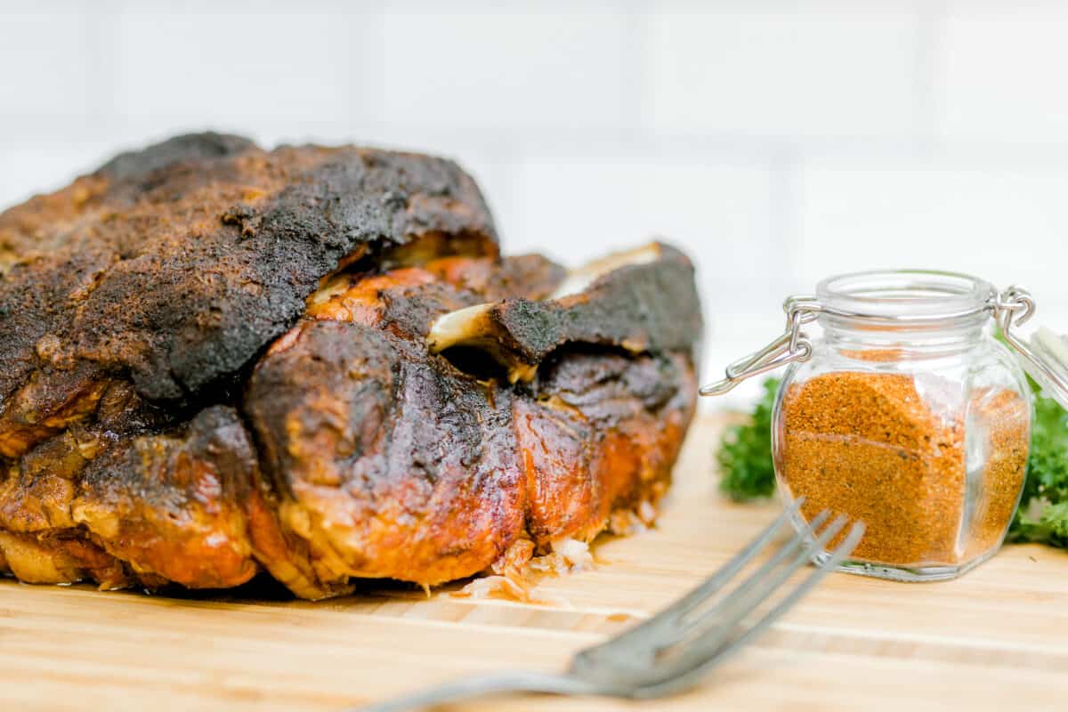 A Smoked Pulled Pork on a wooden cutting board along side a jar of my Best BBQ Rub.