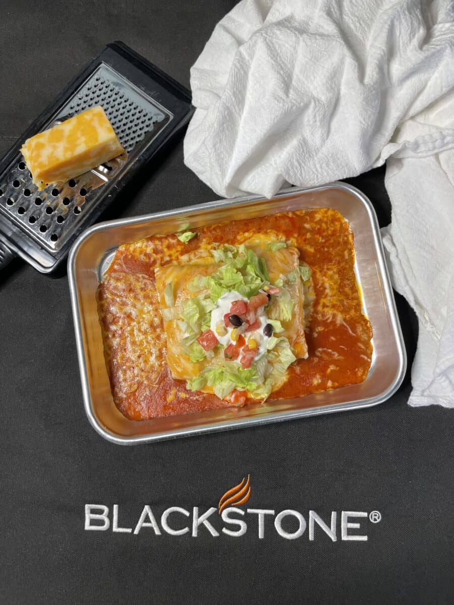 Blackstone Pulled Pork Burritos (Wet) on a small sheet pan along with a cheese grater, block of Colby cheese and a white linen napkin and the Blackstone logo.