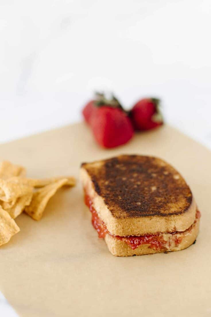 Grilled Peanut Butter and Jelly on a board with a side of chips and fresh strawberries.