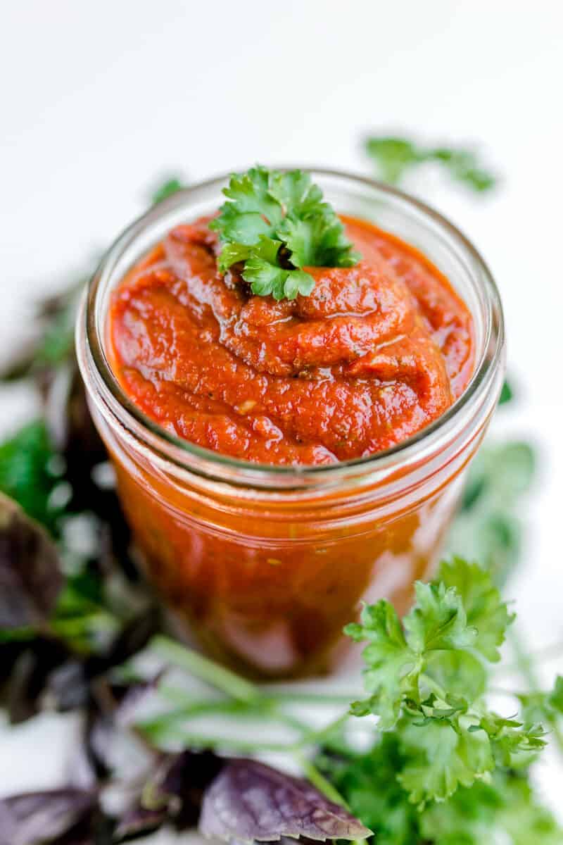 A Jar of Best Pizza Sauce surrounded by fresh herbs