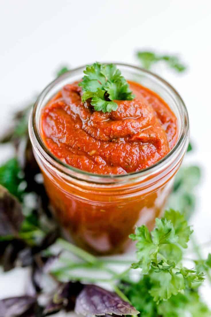 A Jar of Best Pizza Sauce surrounded by fresh herbs.