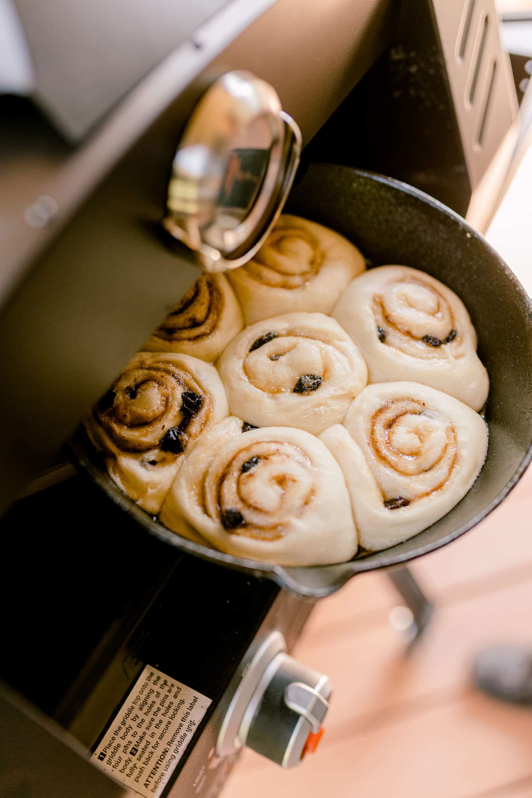 Unbaked cast iron pan of homemade cinnamon rolls being placed into a hot pizza oven.