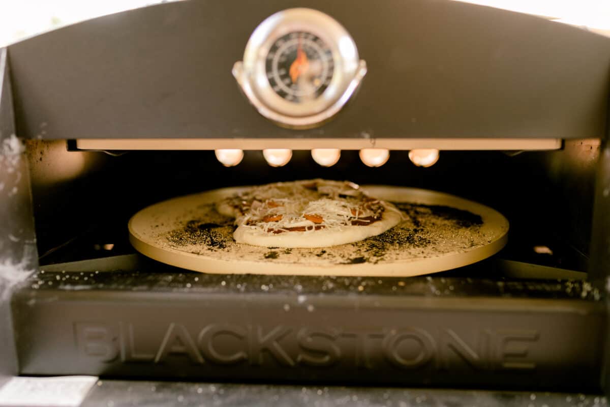 Temperature Gauge on the front of the Pizza Oven along with a pizza cooking on the inside of the oven.
