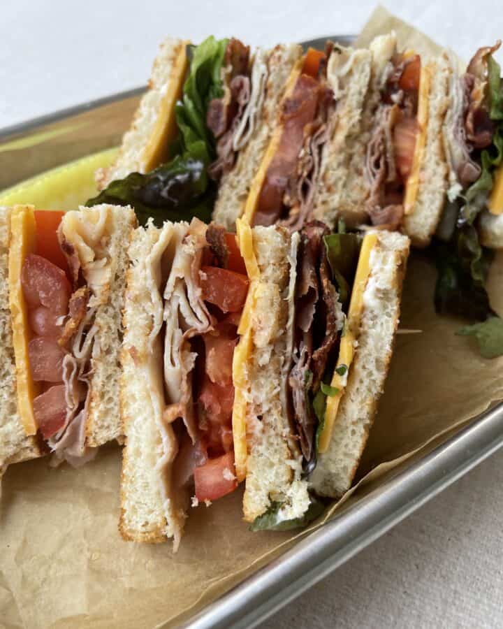 A Classic Club Sandwich on a serving tray with a dill pickle.