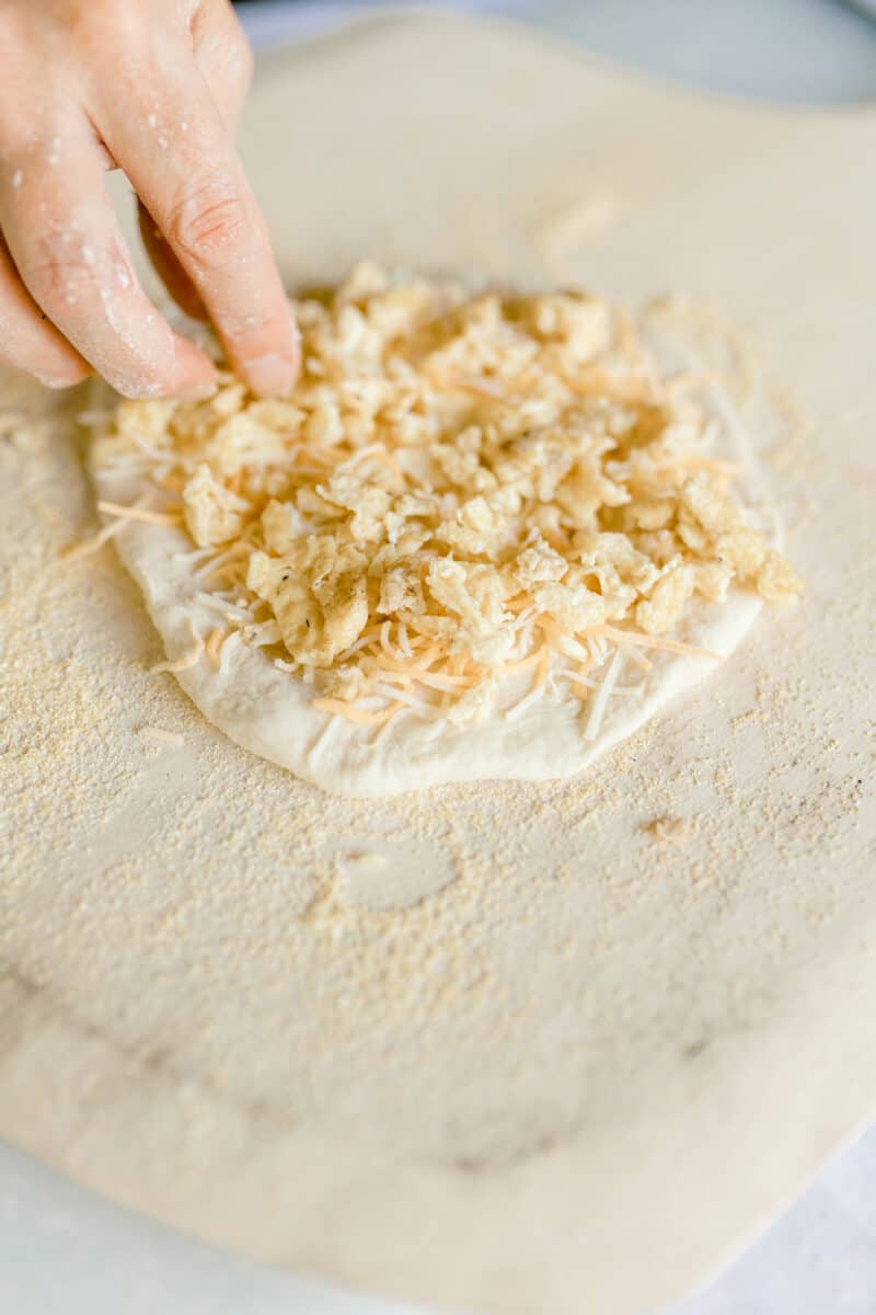 Spreading shredded cheese and scrambled eggs on top of pizza dough.
