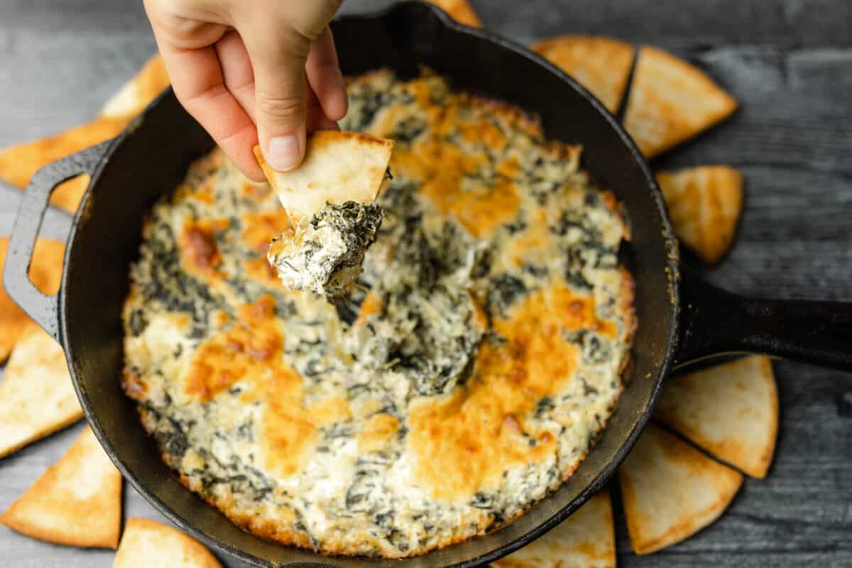 Homemade Baked Triangle Chips Surrounding Smoked Hot Spinach Artichoke Dip in a Cast Iron Pan.