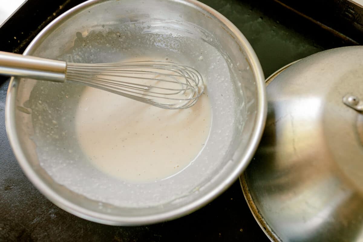 Making Alfredo Sauce on a Blackstone Griddle in a metal pan with a whisk.