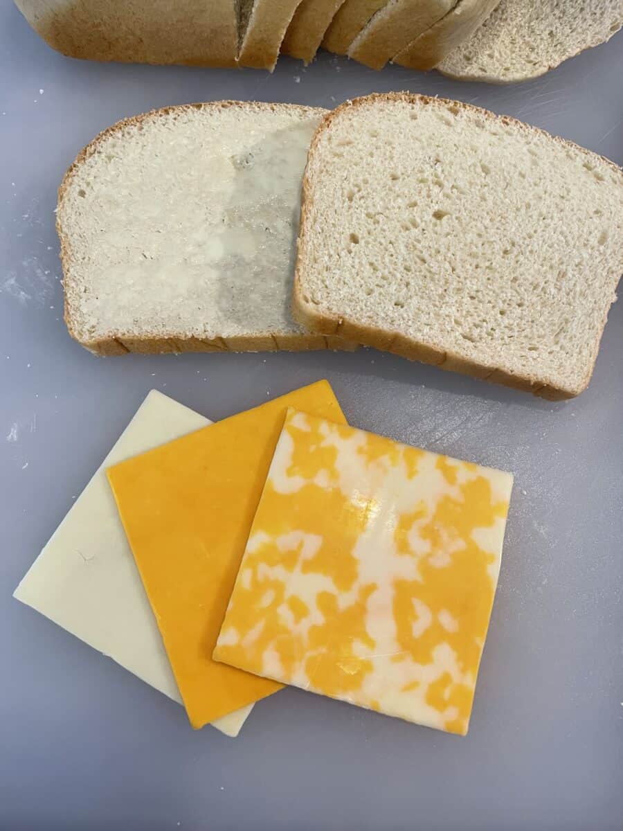 Ingredients for a Grilled Cheese Sandwich - 3 slices of different cheeses and 2 slices of homemade white bread that is butter on one side.  