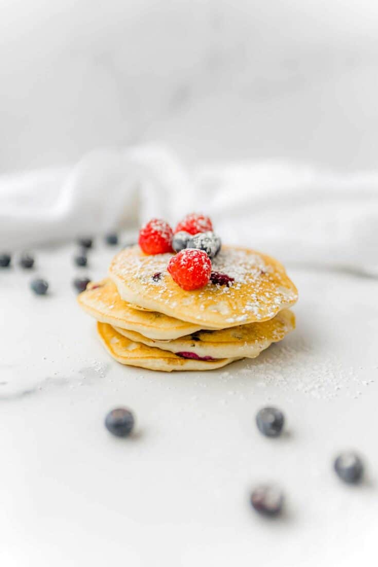 A Stack of Blueberry Pancakes made with Bisquick topped with powdered sugar, fresh raspberries and blueberries.