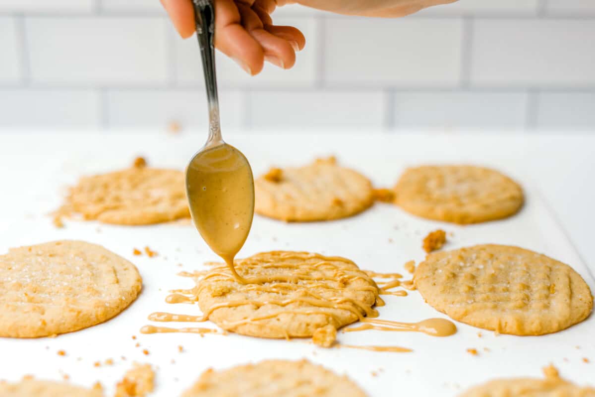 Drizzling Melted Peanut Butter over Double Peanut Butter Cookies Recipe on a piece of parchment paper.
