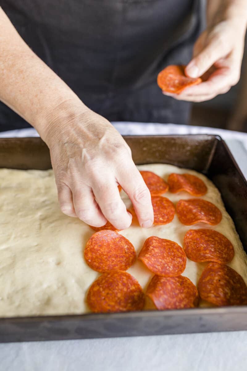 Adding Slices of Pepperoni on top of the Pizza Dough.