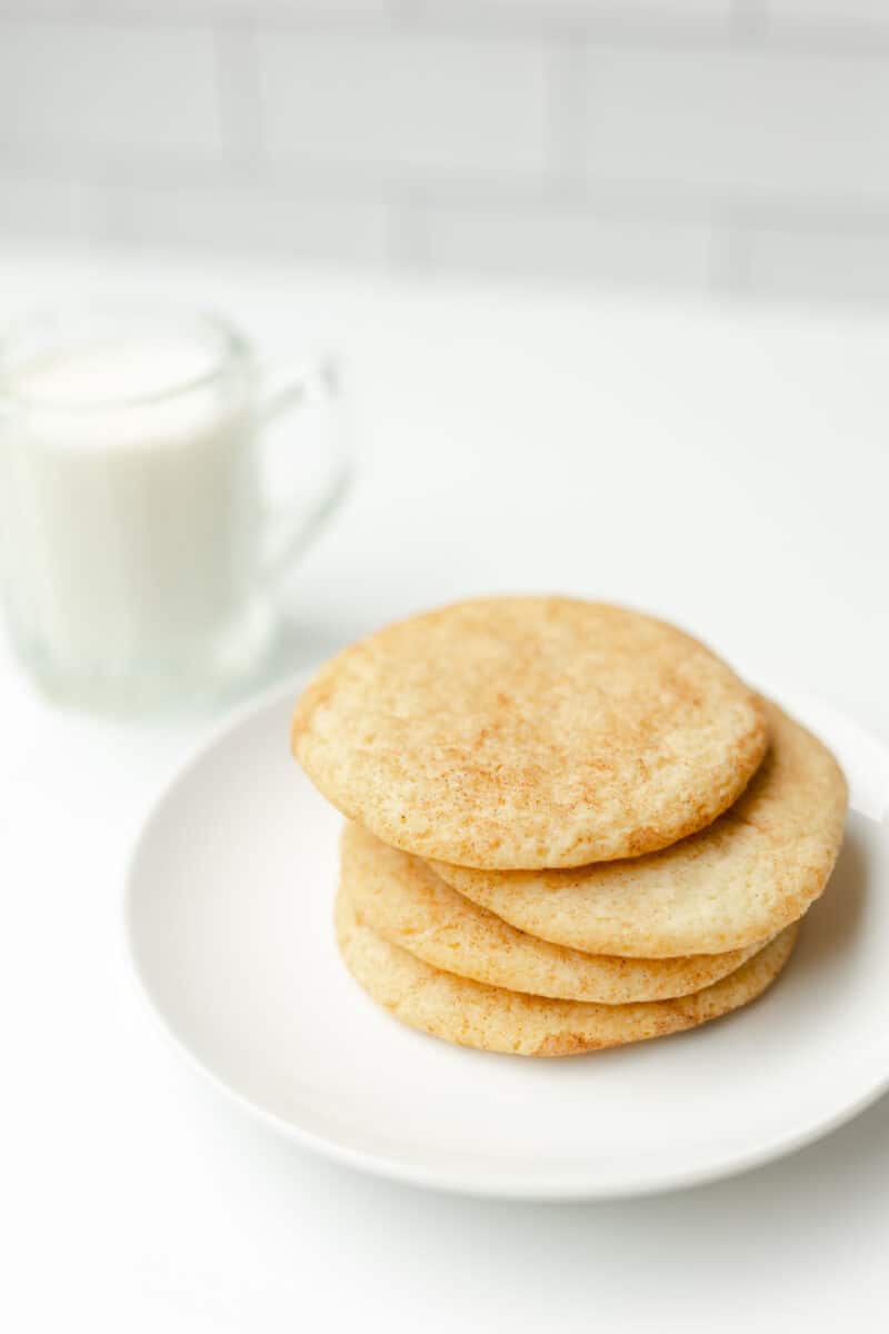 A Stack of Snickerdoodles on a White Plate with a tiny glass of milk.