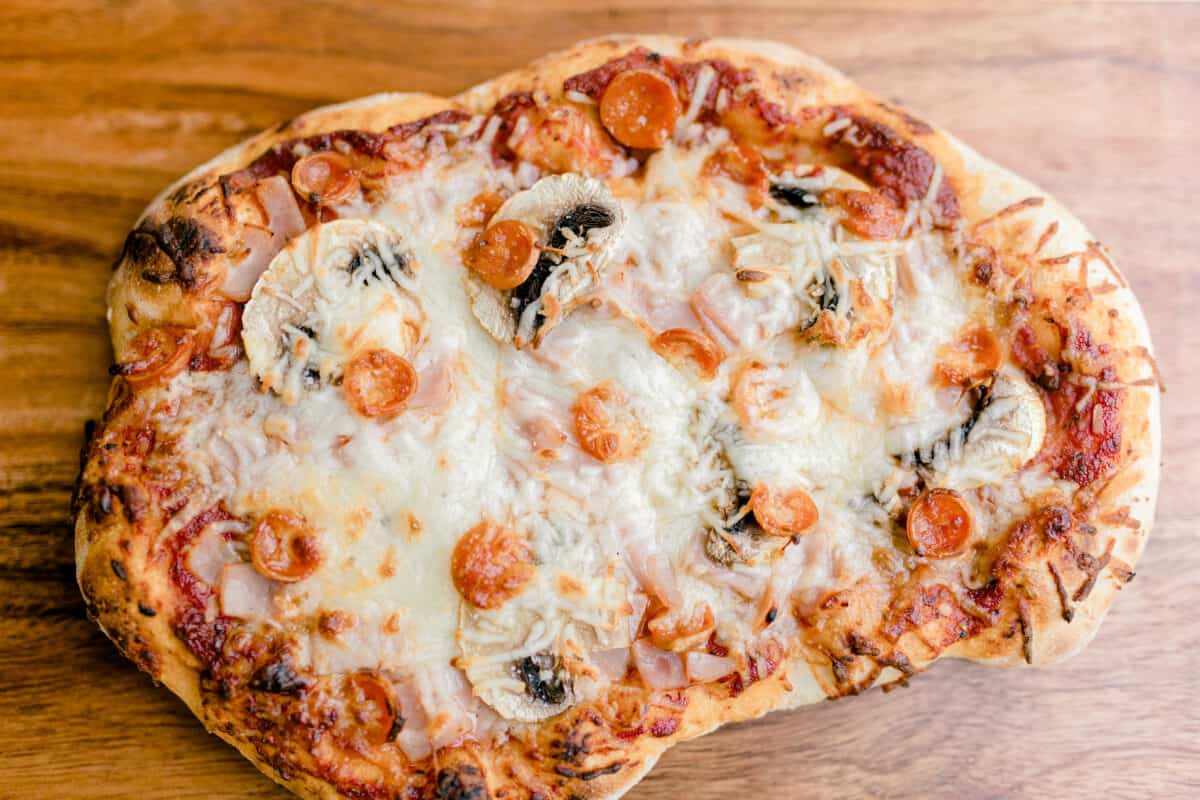 A Whole Pepperoni Mushroom Pizza with Ham on a Wooden Board.