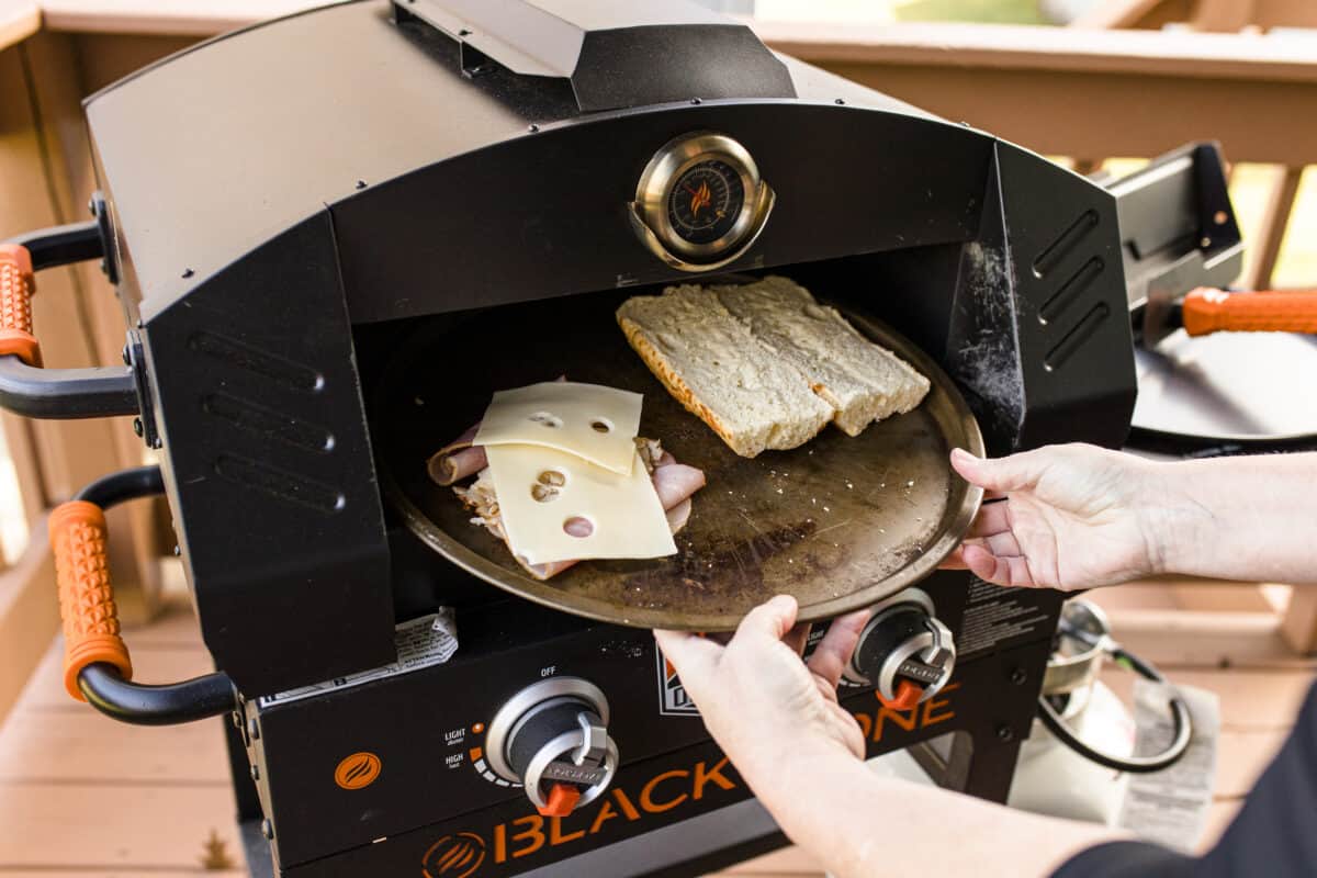 Placing a Pizza Pan of a Ham and Turkey Sandwich Ingredients into a Blackstone Pizza Oven.