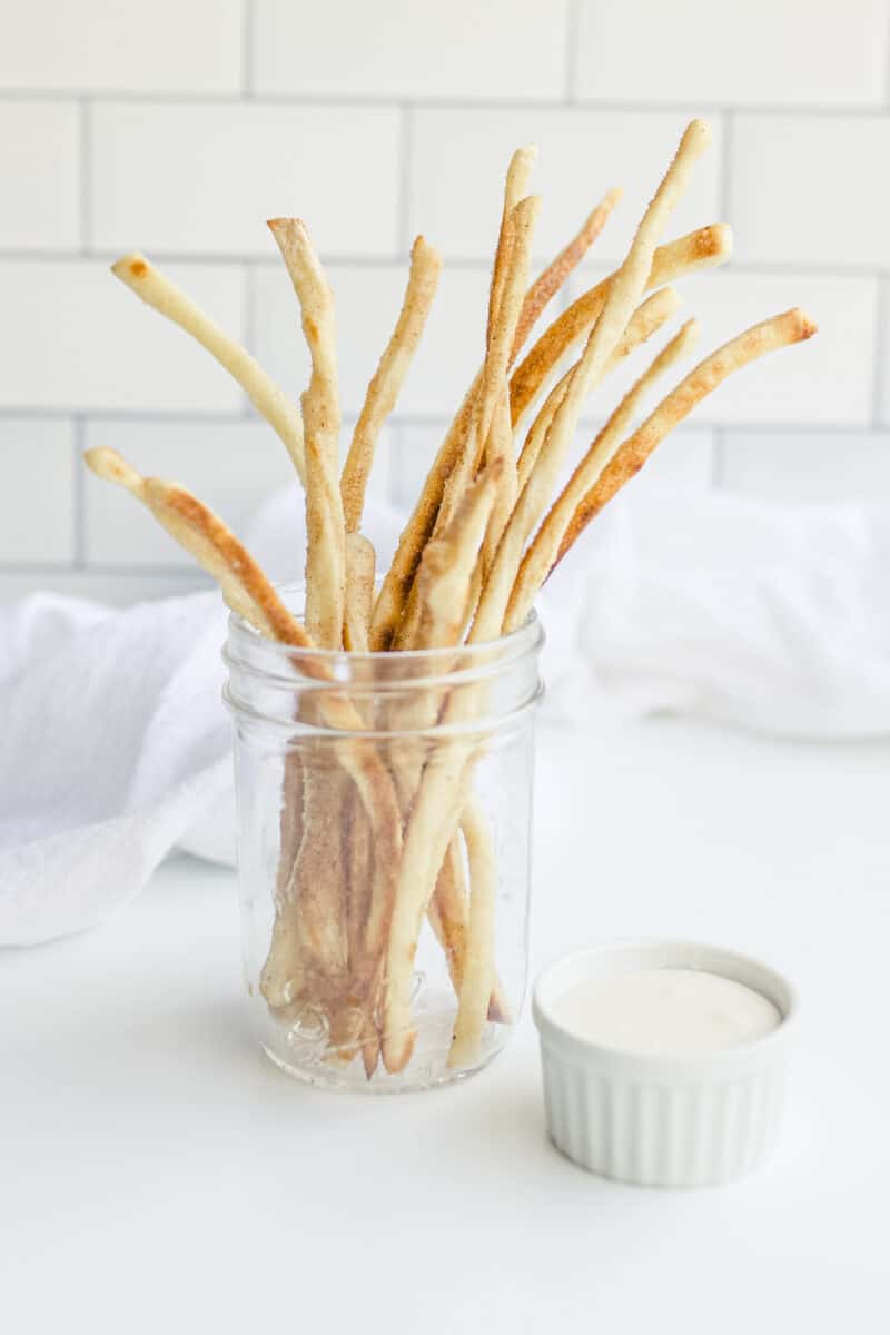 A Jar of Cinnamon Sugar Italian Breadsticks with a side of Icing for Dipping.