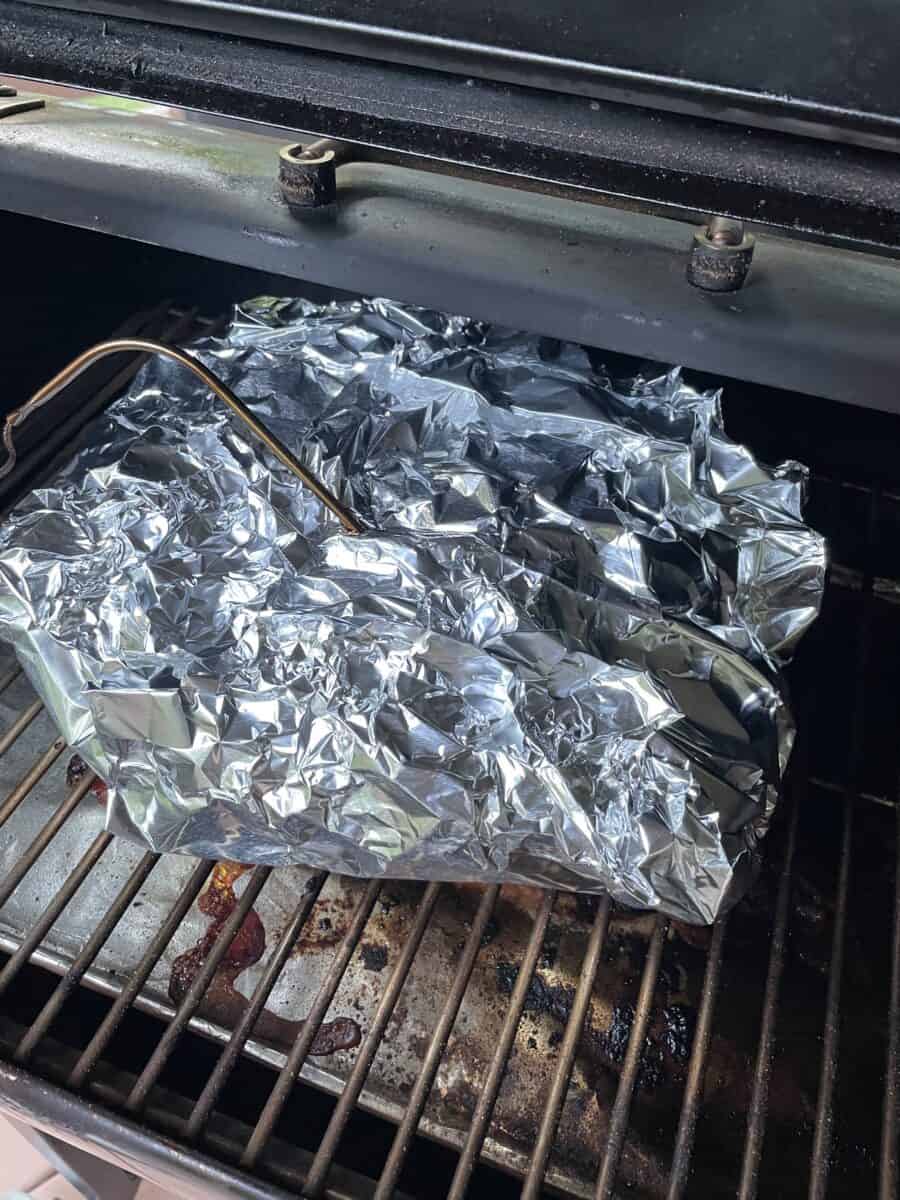 A Foil Wrapped Pulled Pork on the Smoker with a Meat Probe Inserted in it.  