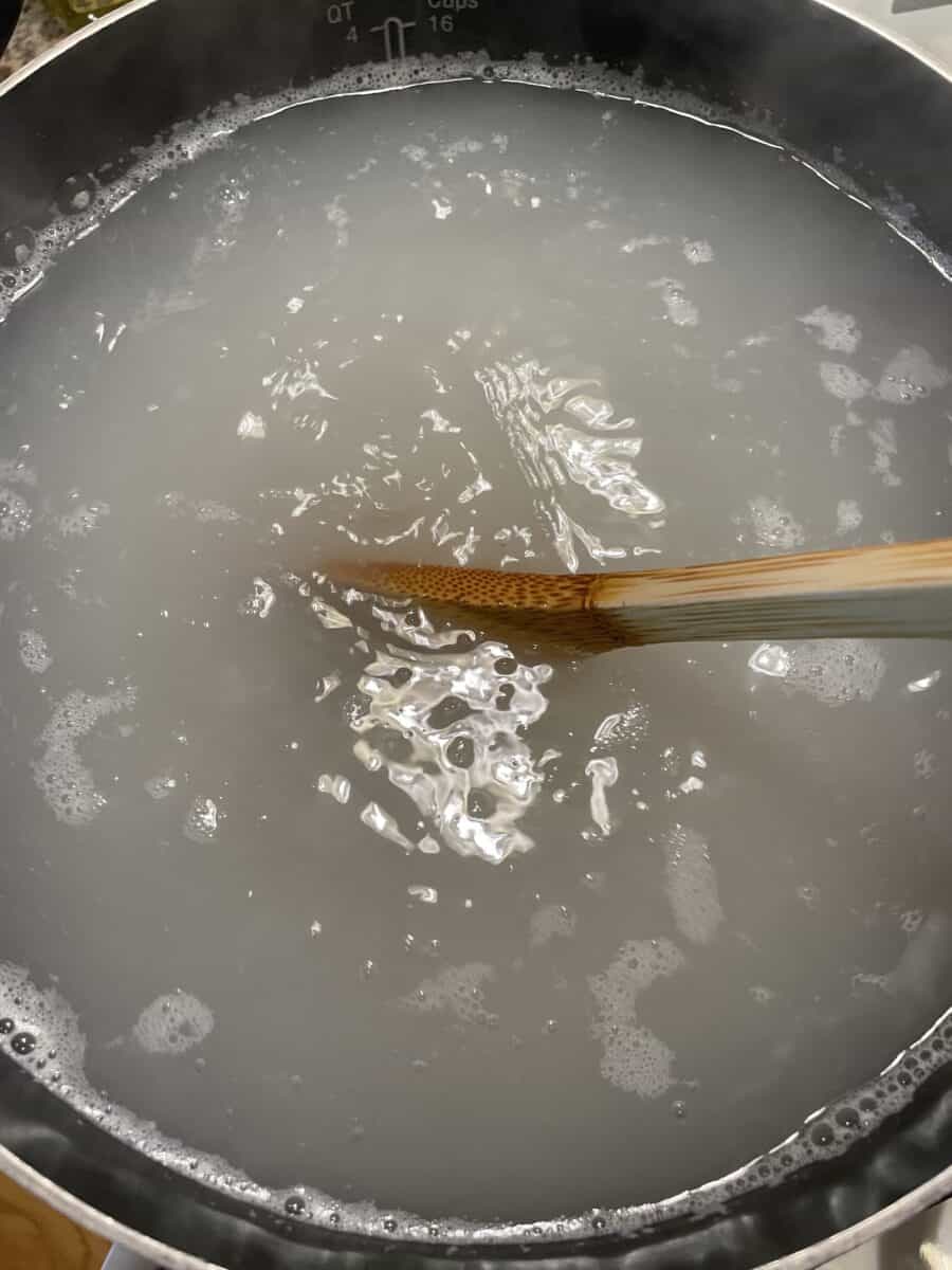 A Large Pot of Boiling Rice Water being stirred by a wooden spoon.