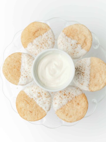 White Chocolate Dipped Snickerdoodles on a Serving Stand with a Bowl of White Melted Chocolate.