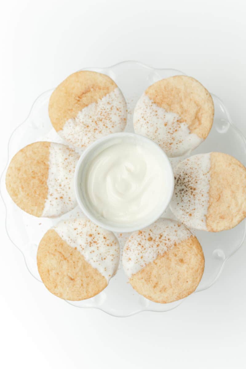 White Chocolate Dipped Snickerdoodles on a Serving Stand with a Bowl of White Melted Chocolate.