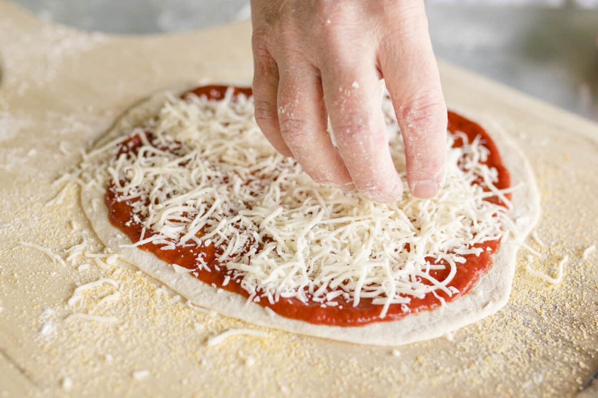 Sprinkling Shredded Cheese on Top of Pizza Sauce Covered Pizza Dough.