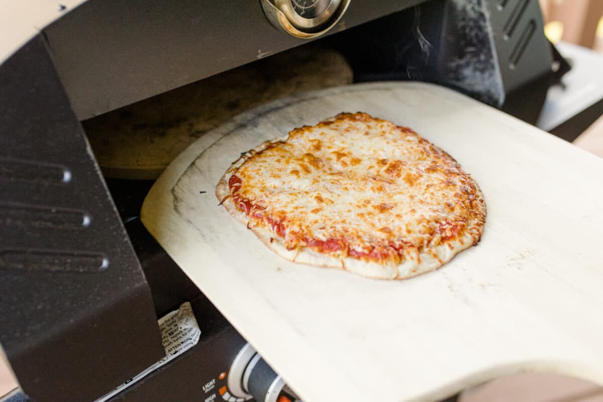 Removing a Homemade Cheese Pizza from the Blackstone Pizza Oven with a Pizza Peel.