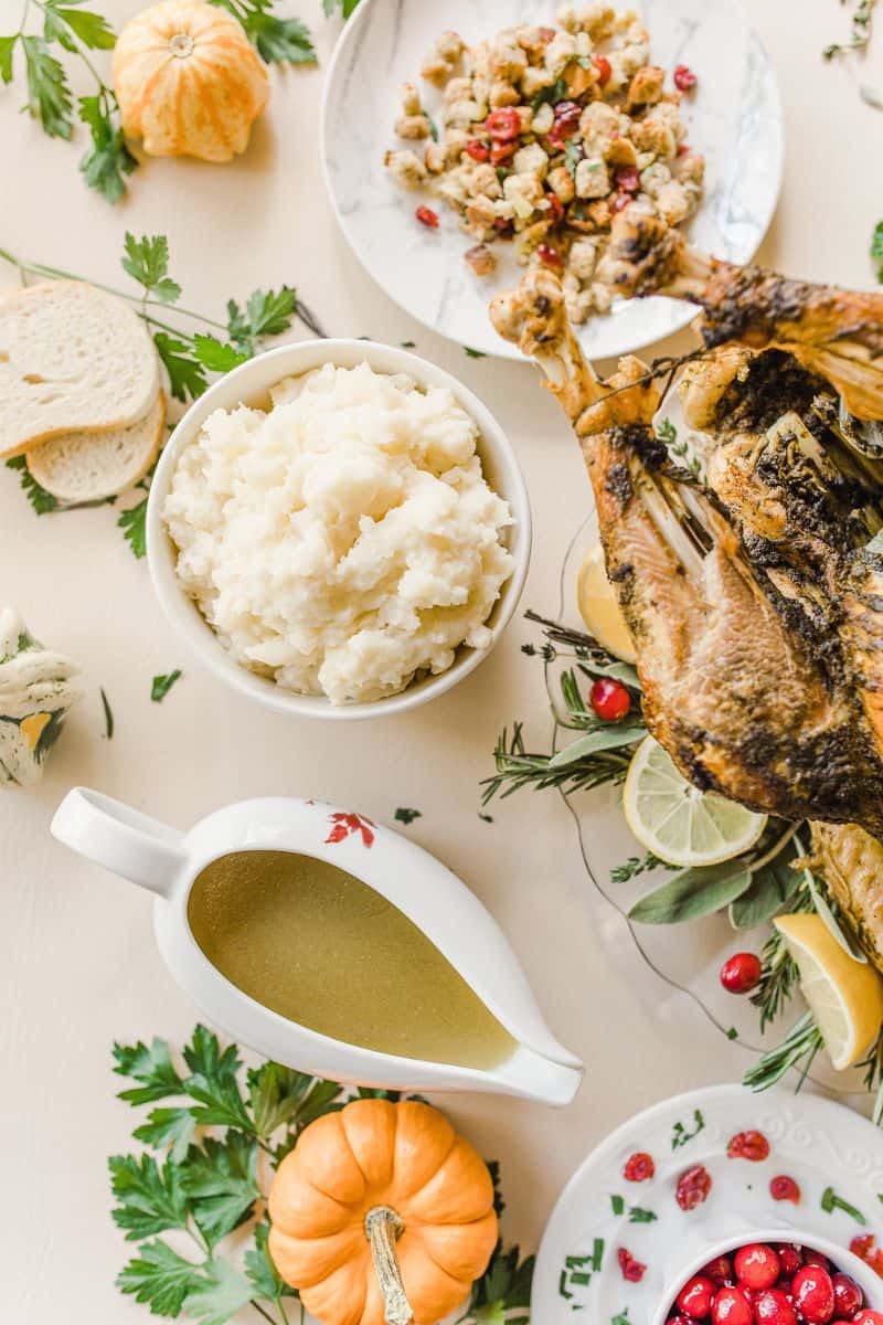 Mashed Potatoes and Gravy on a Thanksgiving Table along with an Roasted Turkey, cranberry stuffing, and a bowl of cranberries.